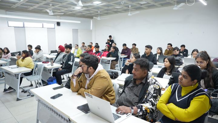 A wider view of a classroom in session, rows of desks running back from the front, most of the seats taken. Every head in the frame is turned the same way, towards the front of the room and out of shot.